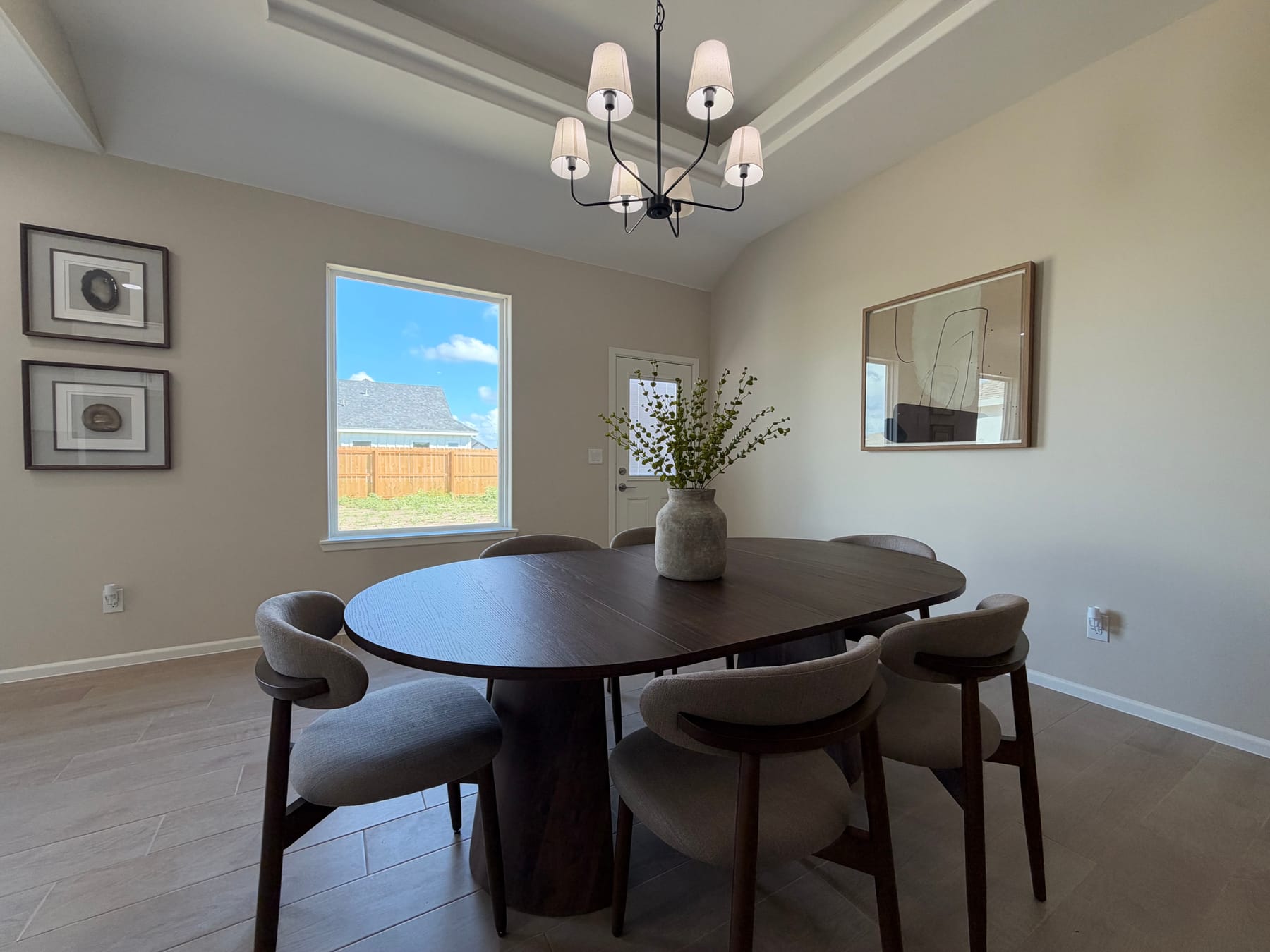 Dining corner with an oval table and upholstered chairs below a window and framed art