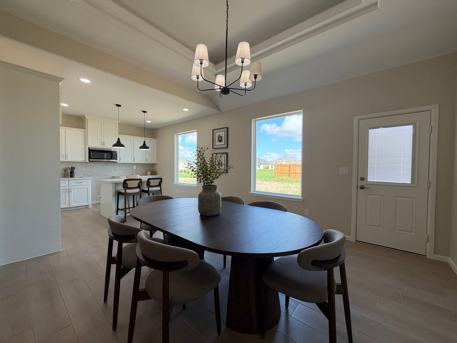 Dining area beside two windows onto the back yard and a back door with a glass panel, with the kitchen island to the left
