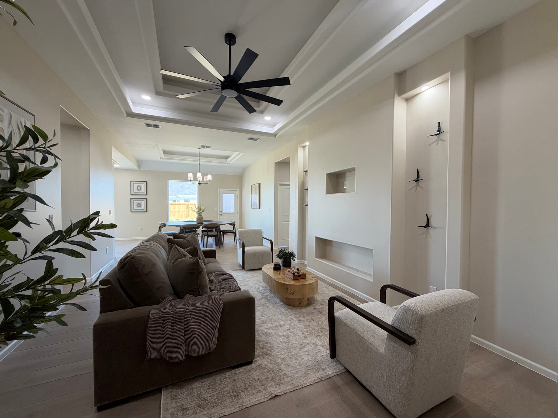 Living room seen past the sofa, with built-in wall niches on the right and the dining area and chandelier beyond
