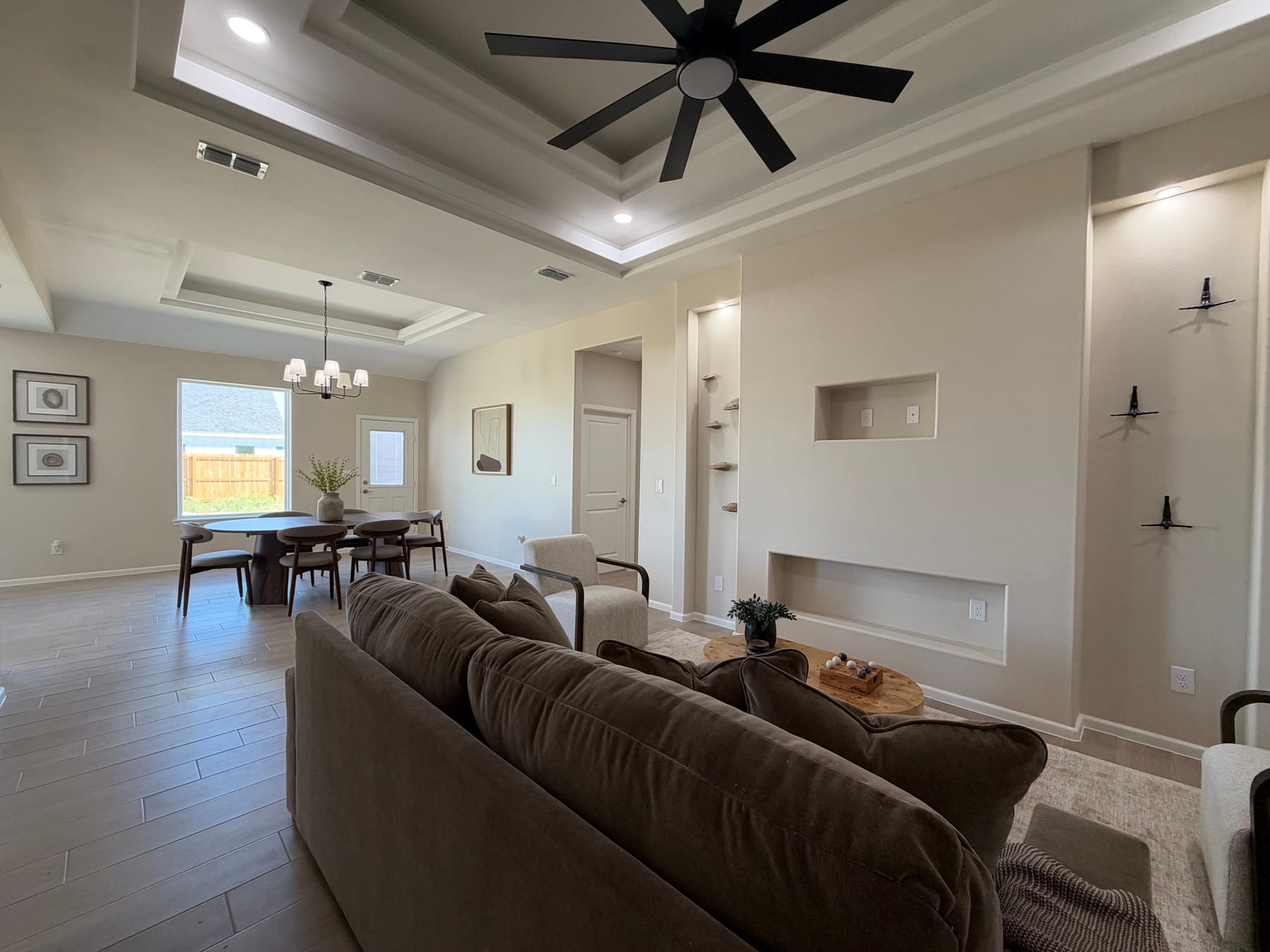 The living room's tray ceiling and black fan above the sofa, looking toward the dining area and its window