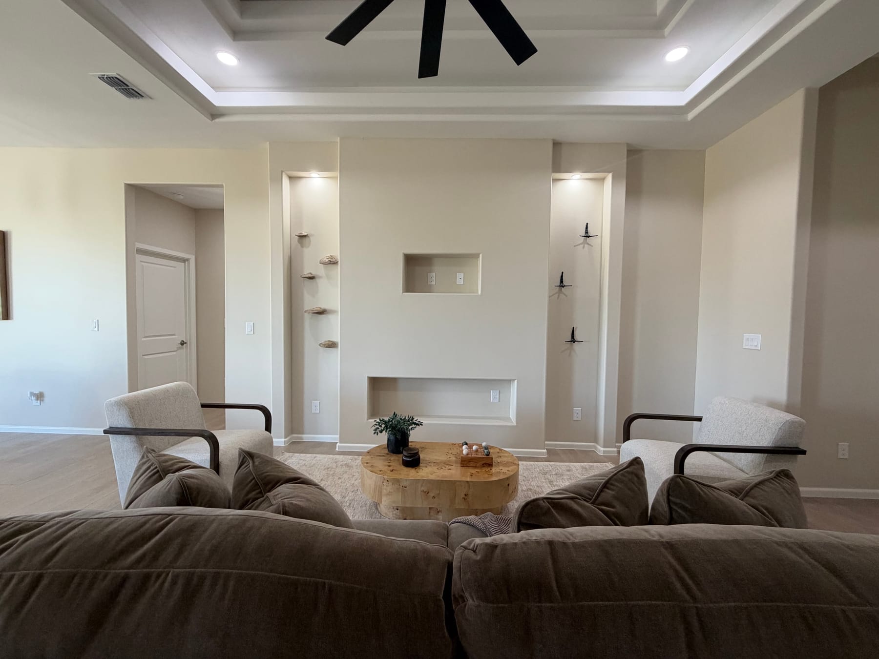 Wall of lit recessed niches with floating shelves and a low media niche between two armchairs, seen from behind the sofa