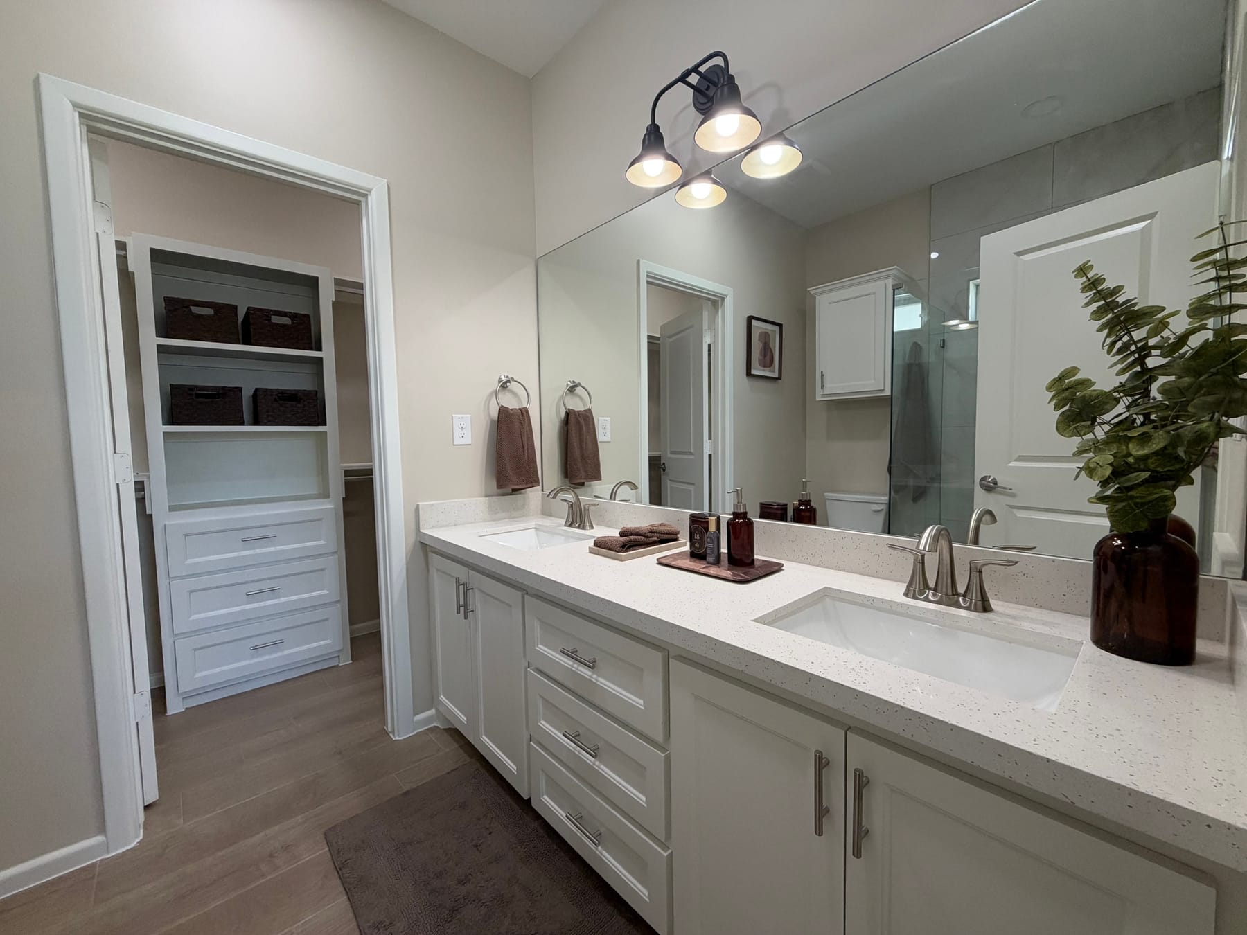 Primary bathroom with a double vanity, a white speckled countertop and a wide mirror, with the walk-in closet's built-in shelves through the doorway