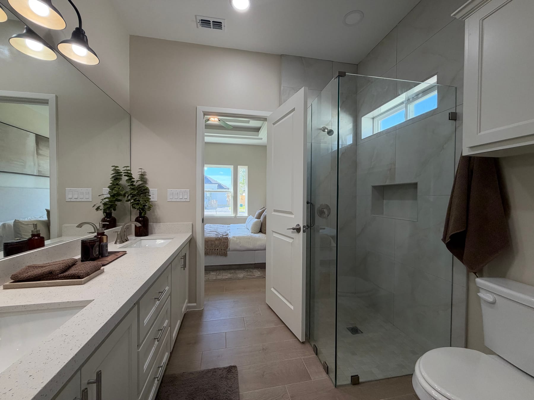 Primary bathroom with a frameless glass walk-in shower, a tiled niche and a high window, looking through to the bedroom