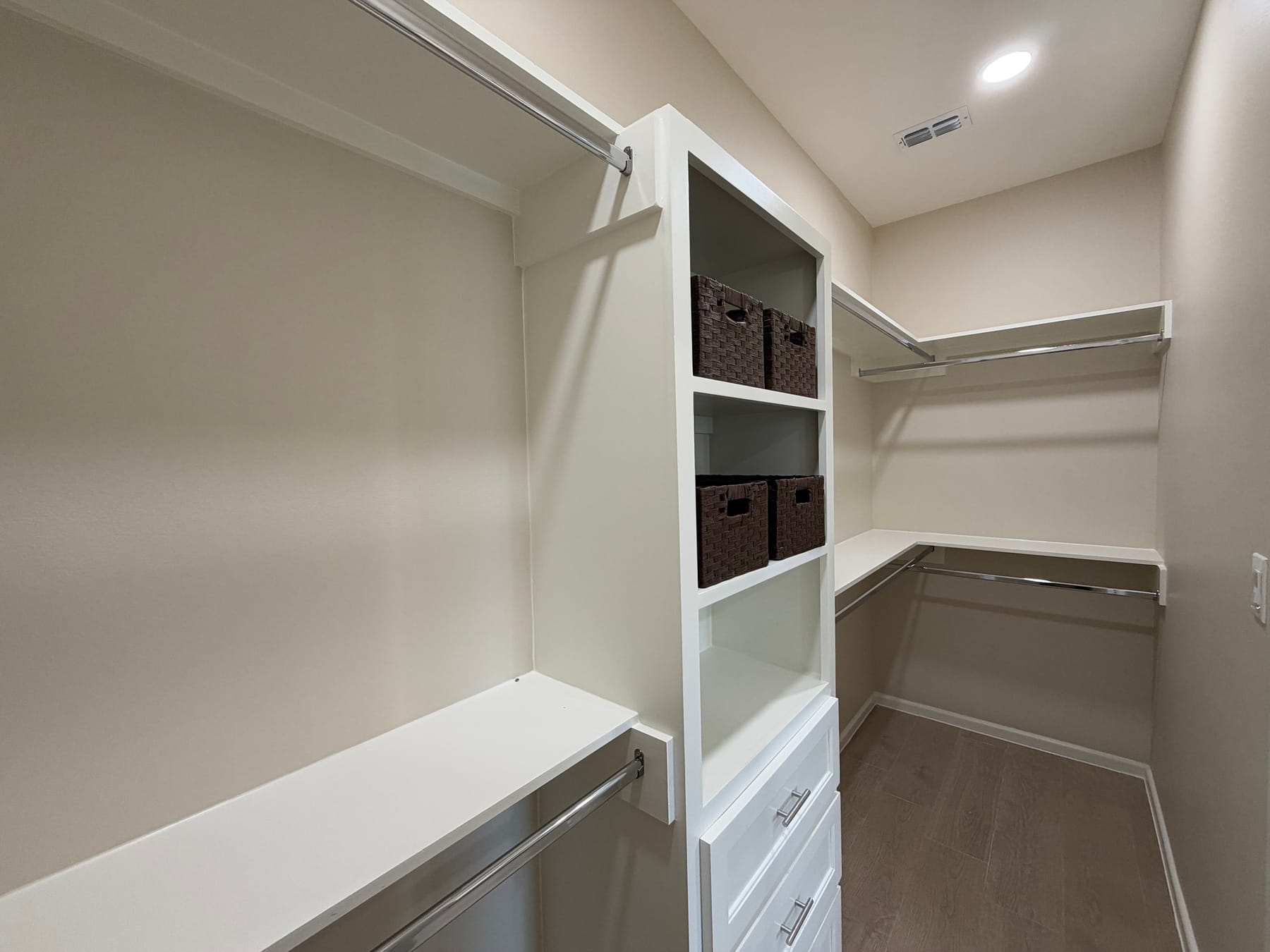Walk-in closet with a white built-in tower of drawers and shelves and hanging rods on two walls
