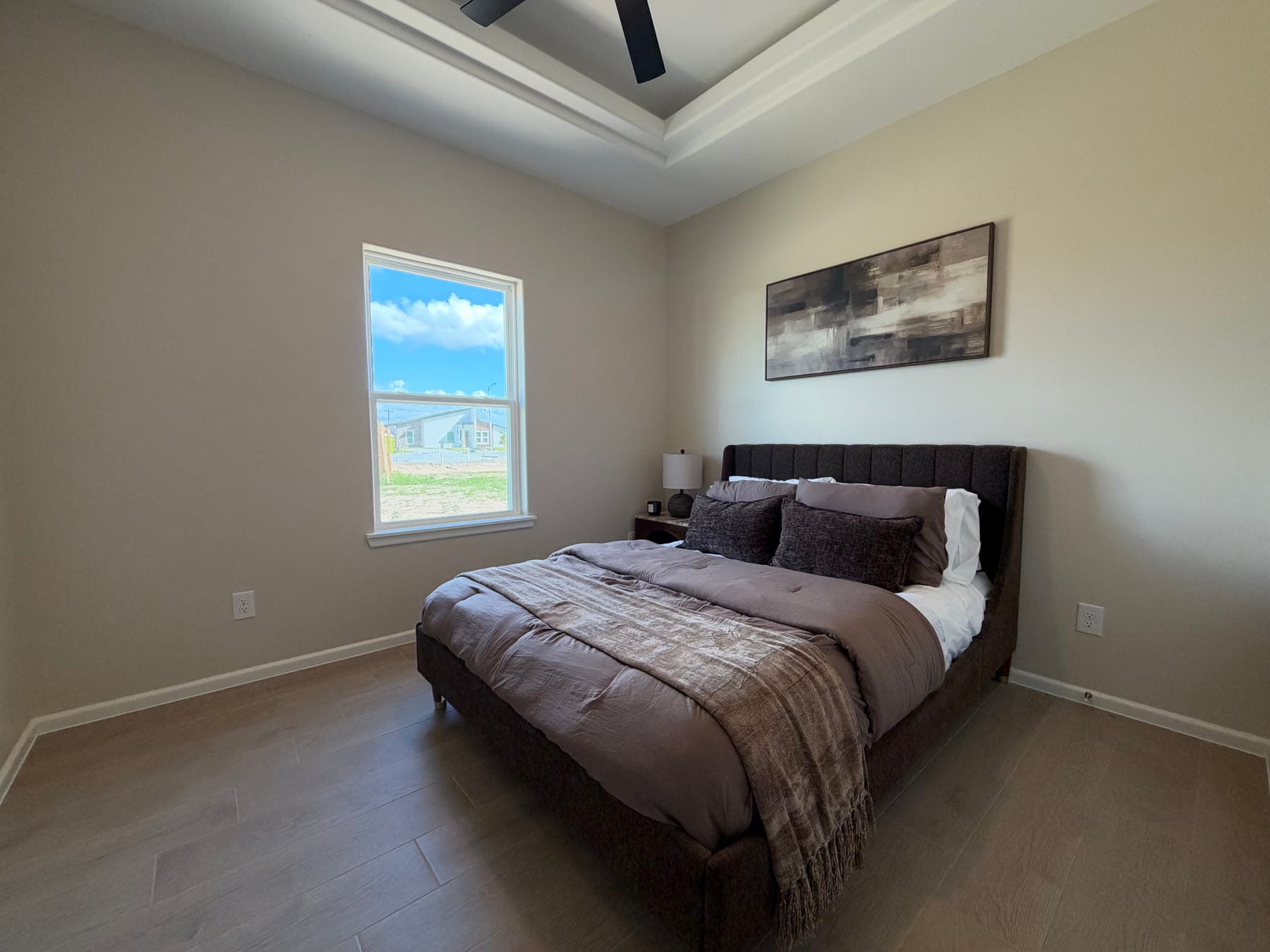 Bedroom with a window, a tray ceiling with a fan and a staged upholstered bed