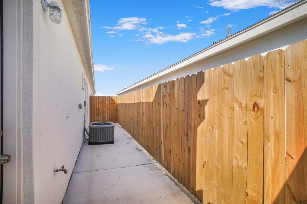 View of the back of a home with fence and air conditioning unit