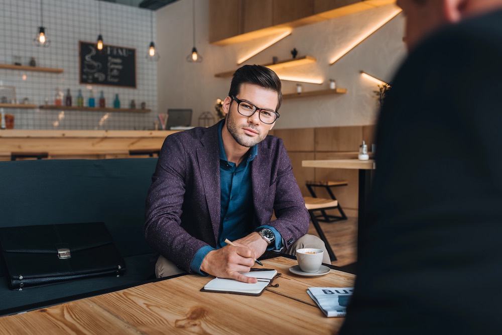 real estate investor looking at the camera and writing notes in a coffee shop